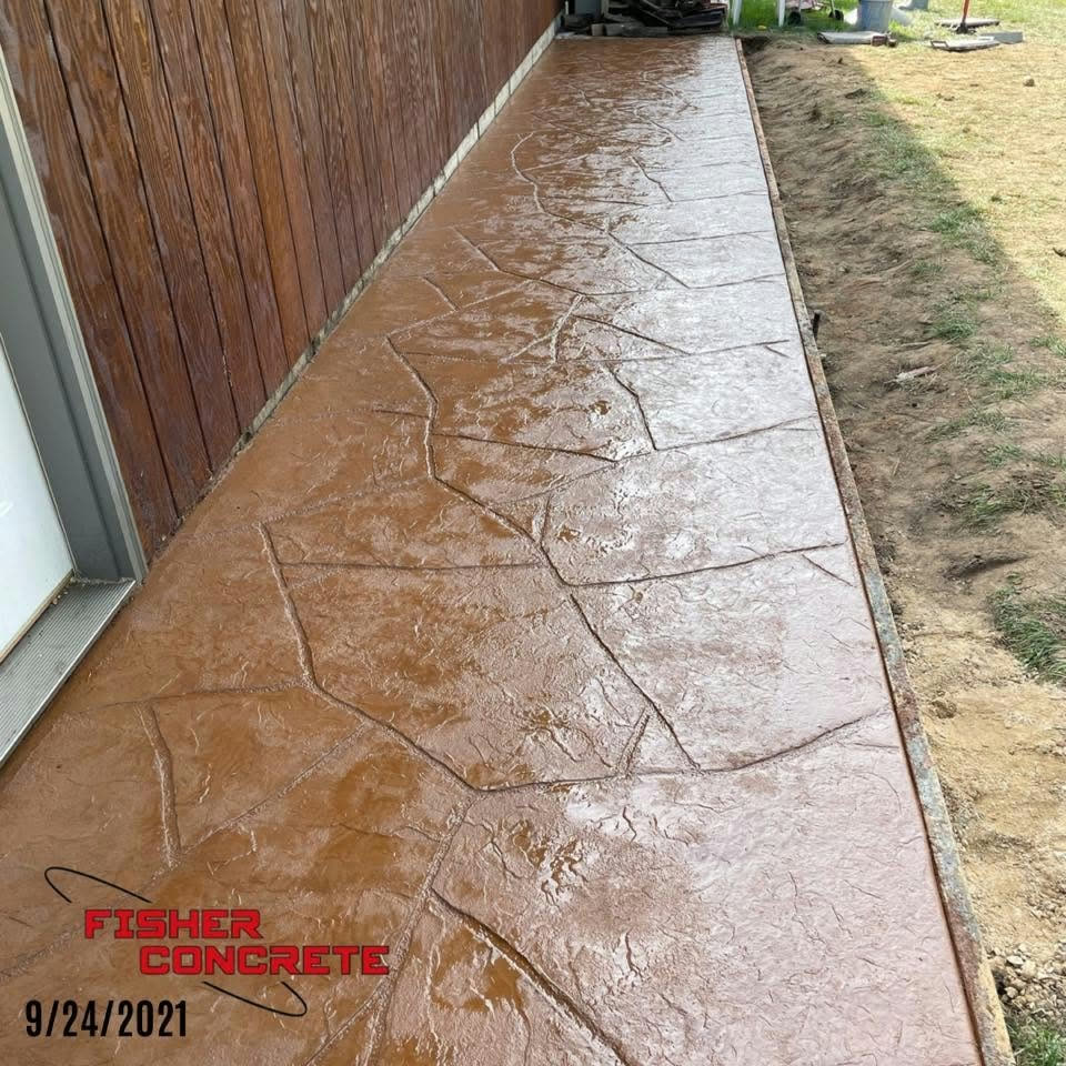 Colored stamped concrete walkway along a wood-sided building